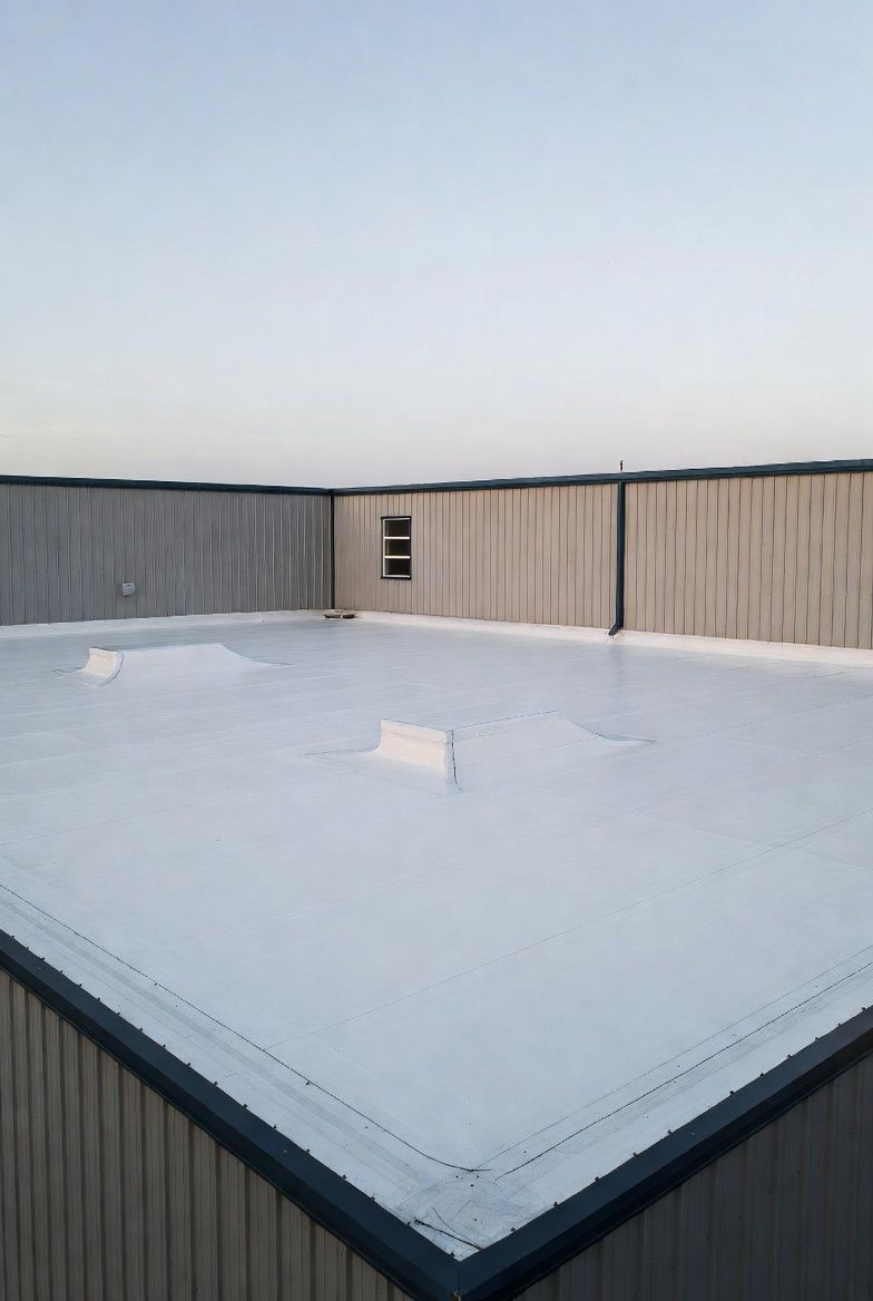 Flat white rooftop with low surrounding wall, small window, clear sky.