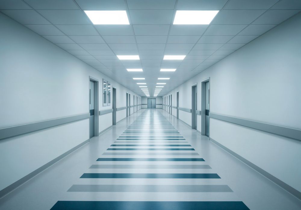 Bright, empty hospital corridor with white walls, blue floor stripes, and overhead lights
