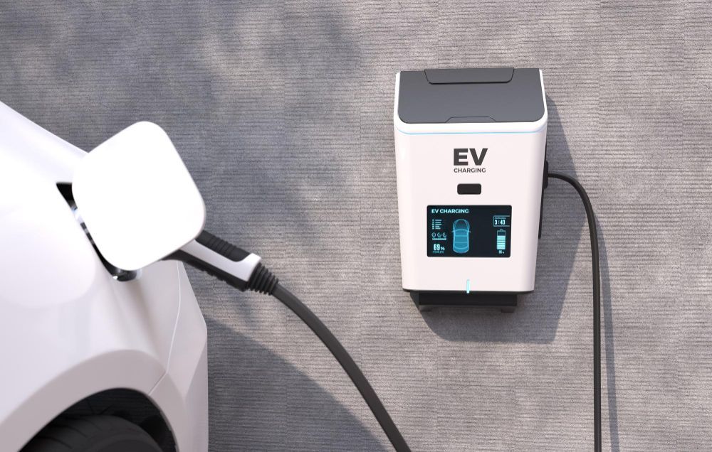 White electric car charging beside a wall-mounted EV charger with a connected cable
