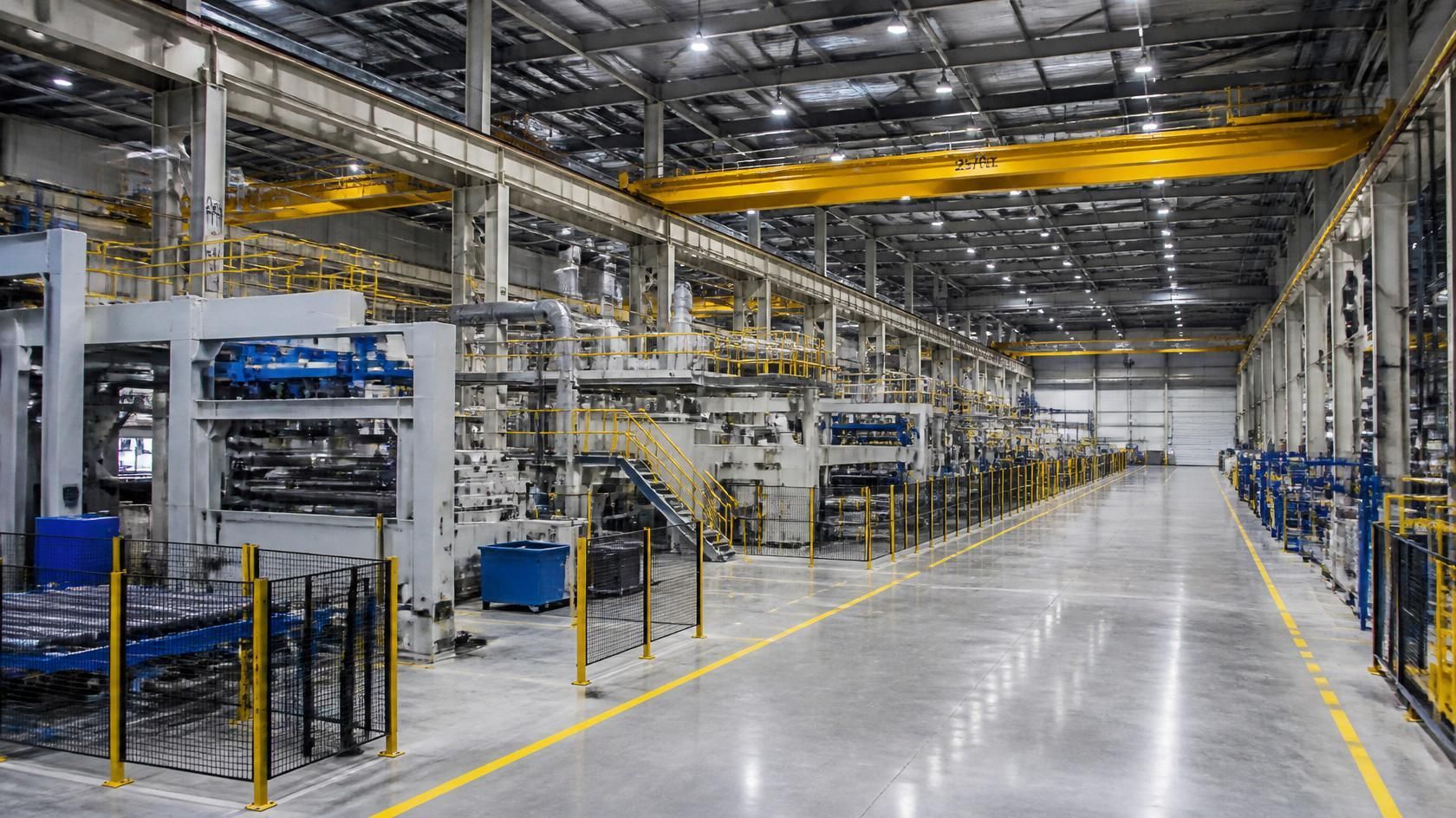 Wide industrial warehouse with metal racks, machinery, and a polished concrete floor under bright overhead lights