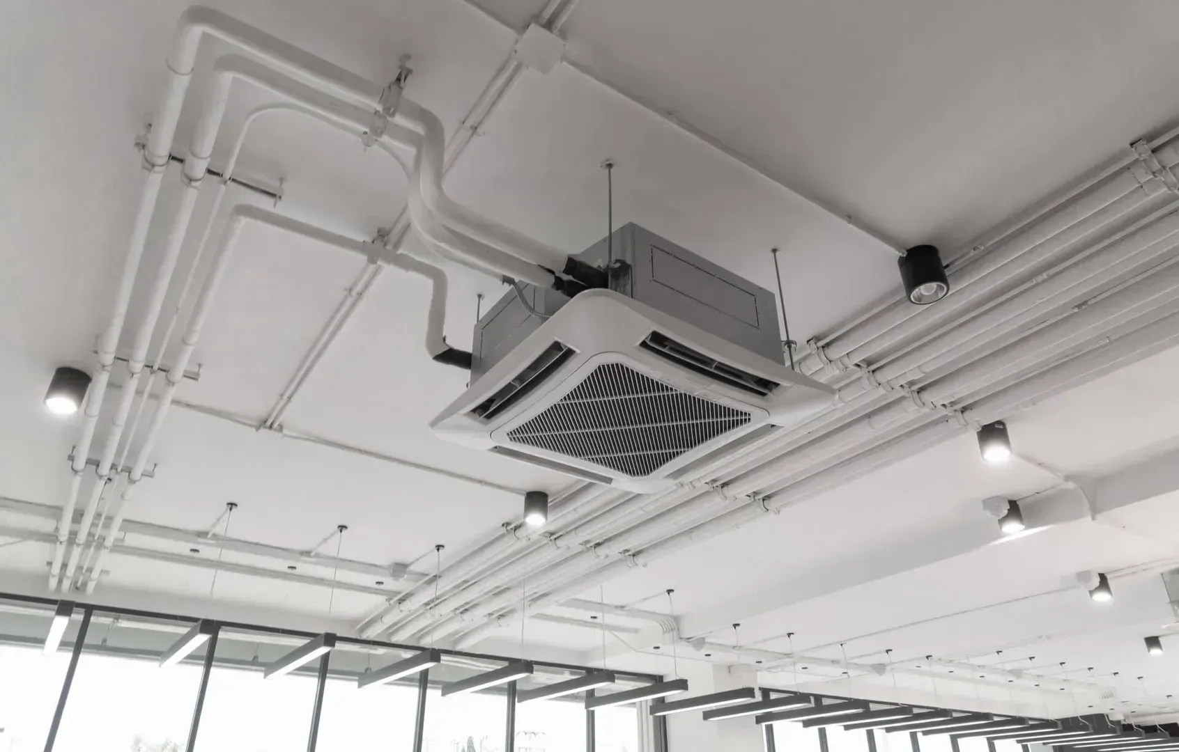 Ceiling-mounted air conditioner and exposed pipes in a bright industrial interior
