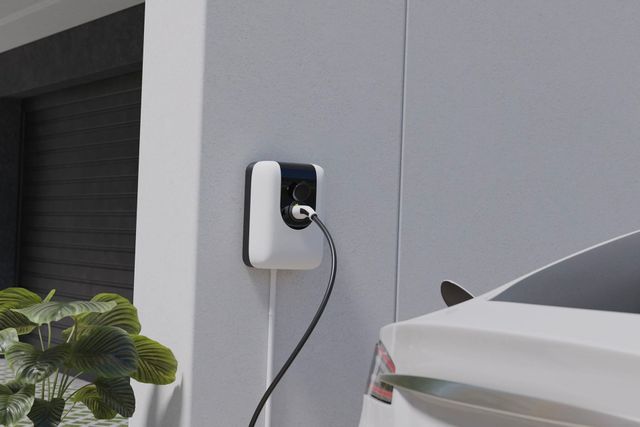 Wall-mounted EV charger plugged into a white car beside a gray garage wall