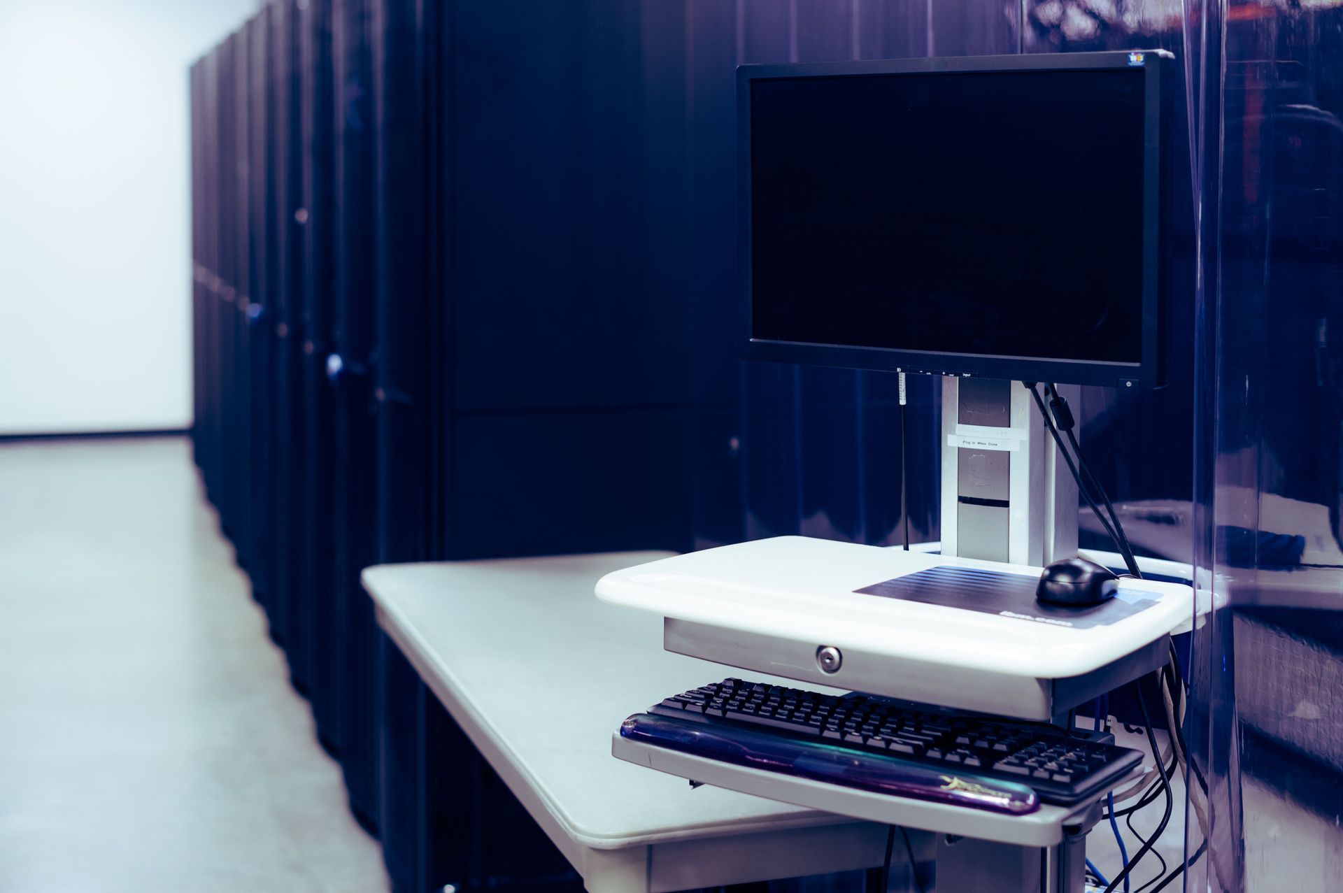 Computer workstation with monitor, keyboard, and cables on a desk in a server room corridor