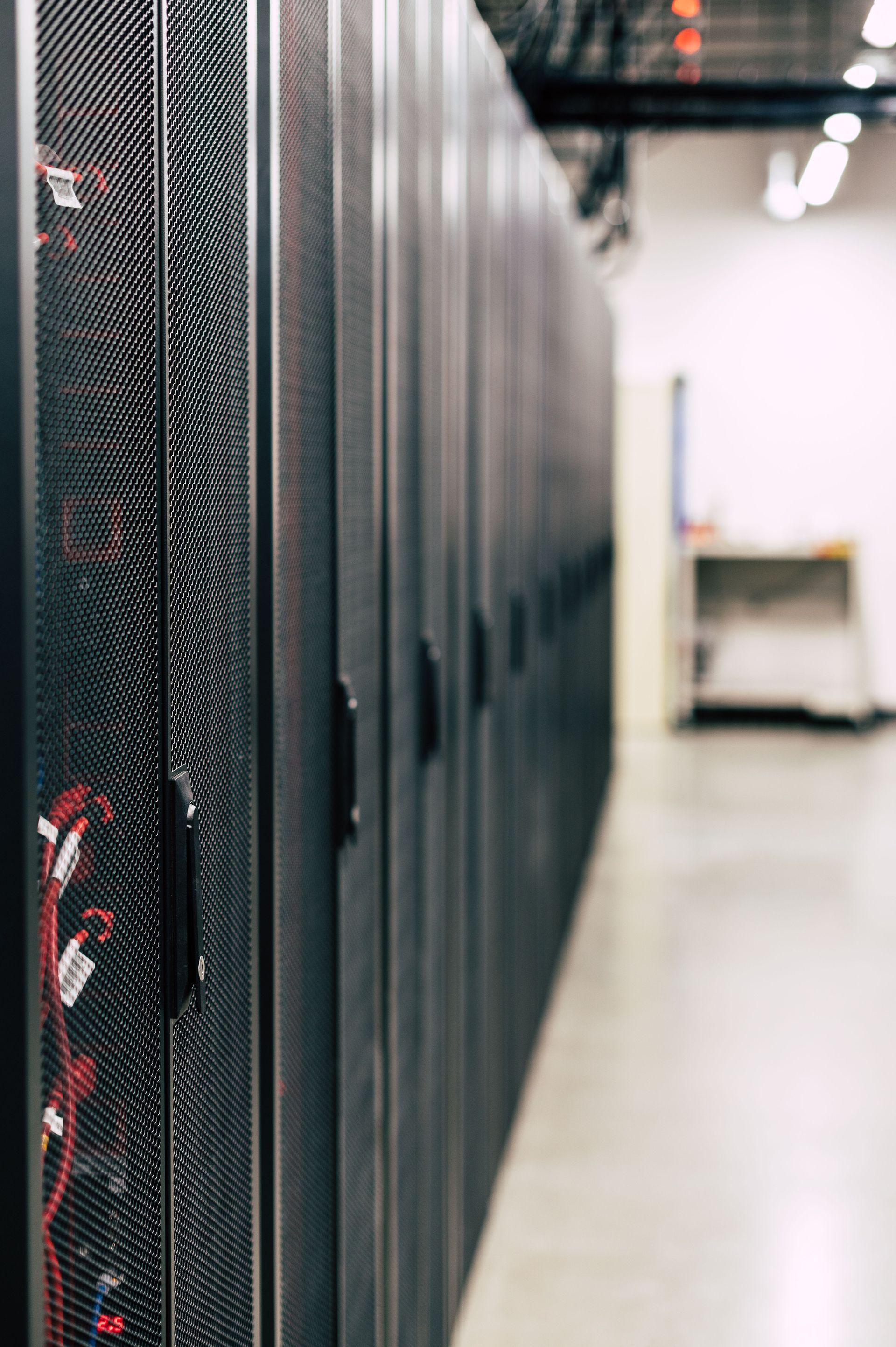 Row of black server racks in a data center hallway, with a blurred cart in the background