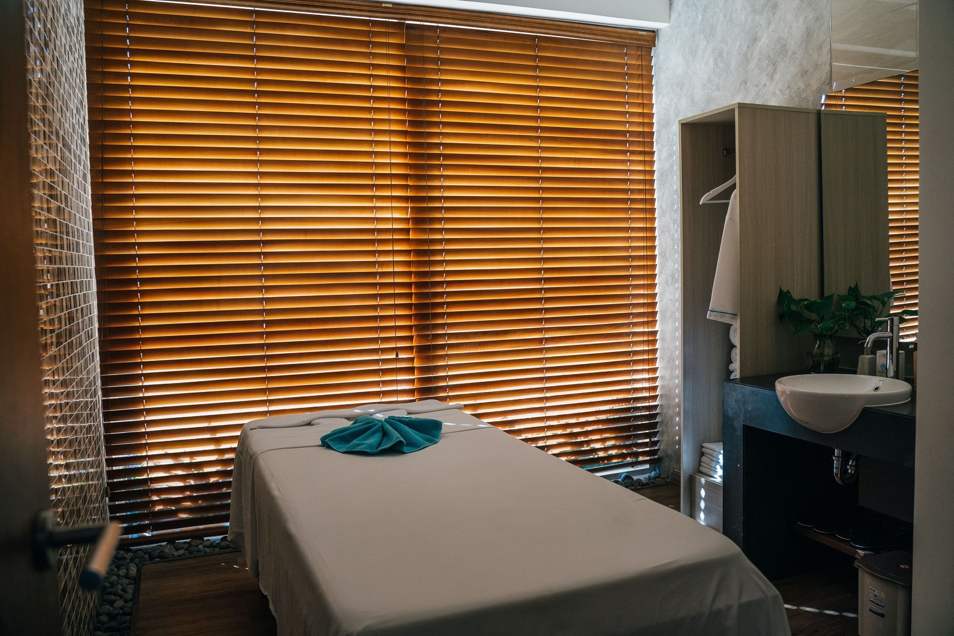 Massage room with treatment table, closed blinds, and a sink in the corner