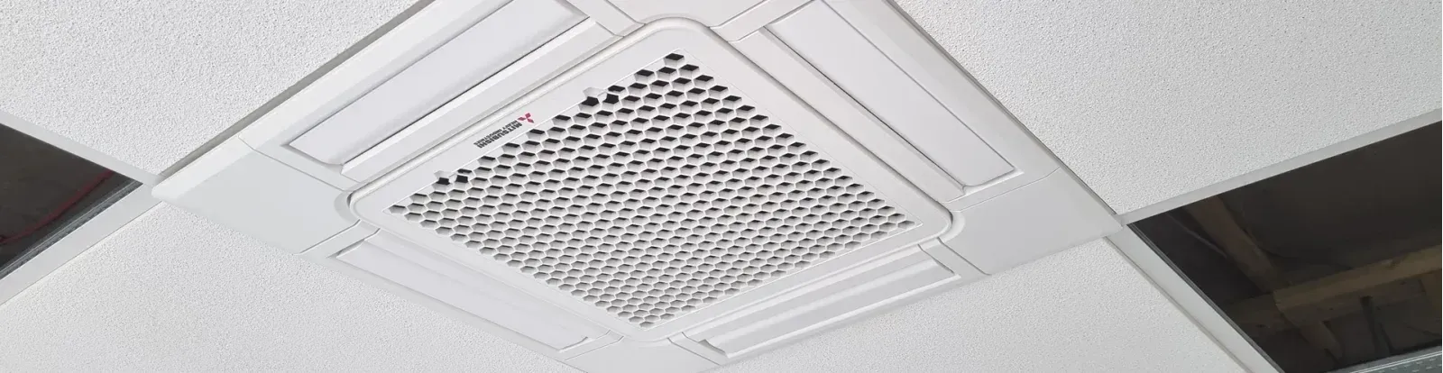 Ceiling ventilation grille set in a white drop ceiling tile with adjacent light panels