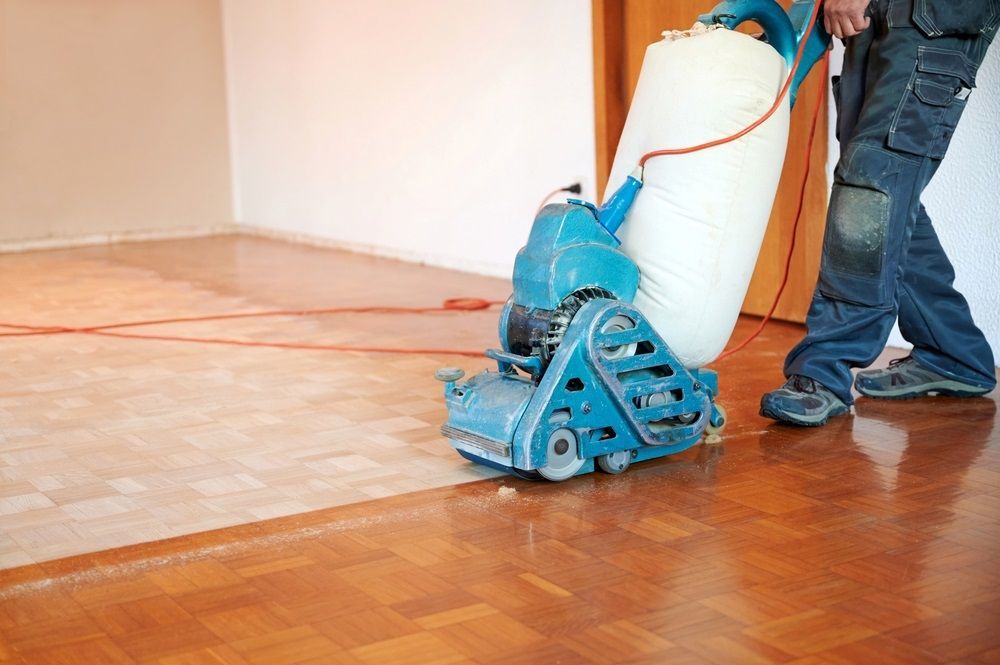 A Man is Sanding a Hardwood Floor With a Machine — Maroochy Floor Sanding in Maroochydore, QLD