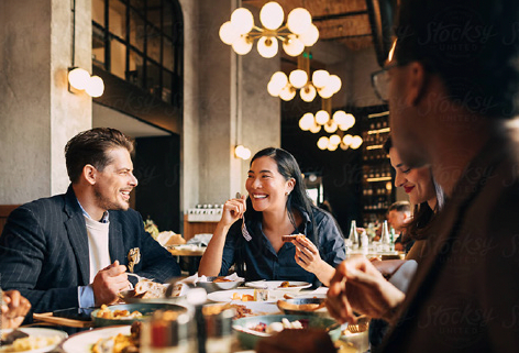 Friends dining and chatting in a warmly lit restaurant with hanging globe lights and drinks on the table.