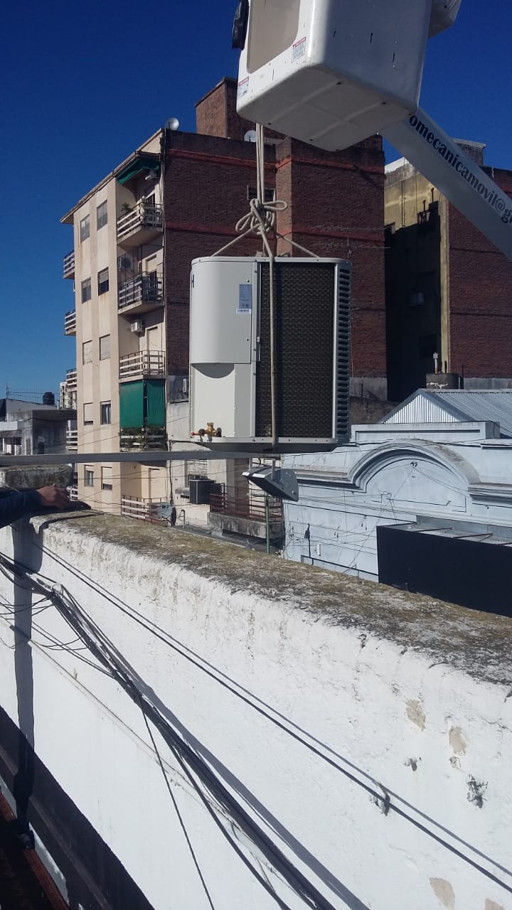 Un hombre en un balde está trabajando en un acondicionador de aire en el techo de un edificio.