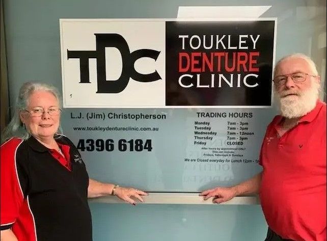 owners of the clinic outside the business shop, showing trading hours — Dentures in Toukley, NSW