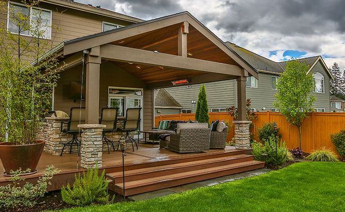 Covered backyard deck with wood steps, wicker seating, stone posts, and a fenced lawn.