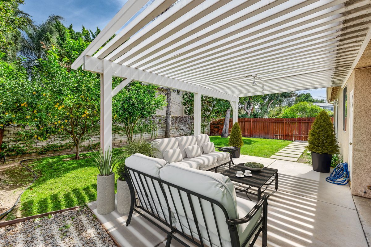 Covered patio with white pergola, cushioned seating, and a green backyard garden.