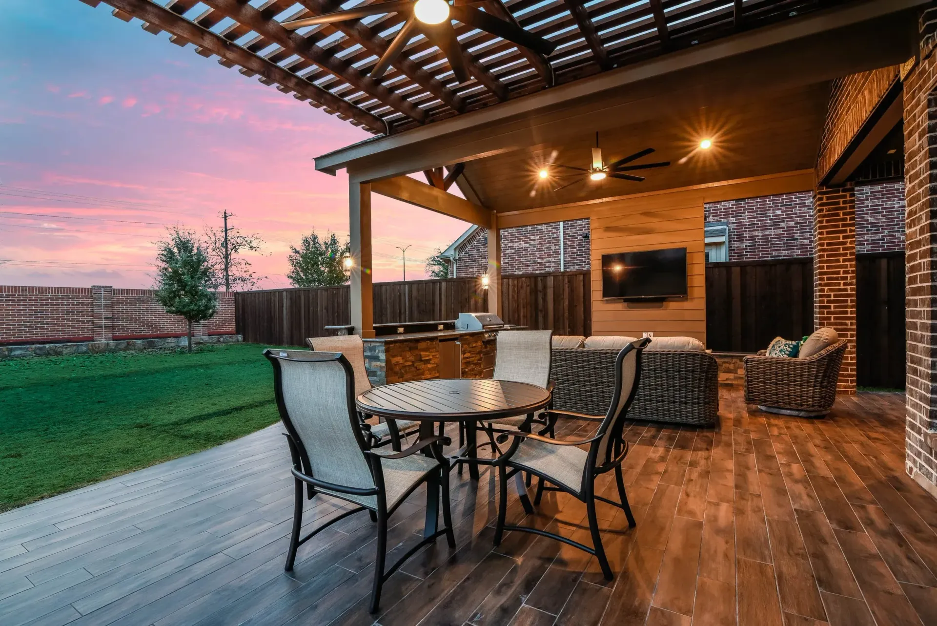 Covered patio with outdoor dining set, string lights, and sunset view over a grassy backyard.