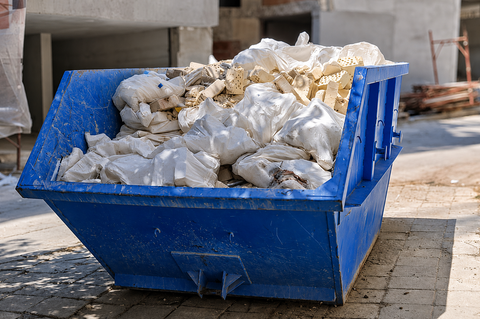 Green dumpster filled with broken white concrete rubble on a sunlit street