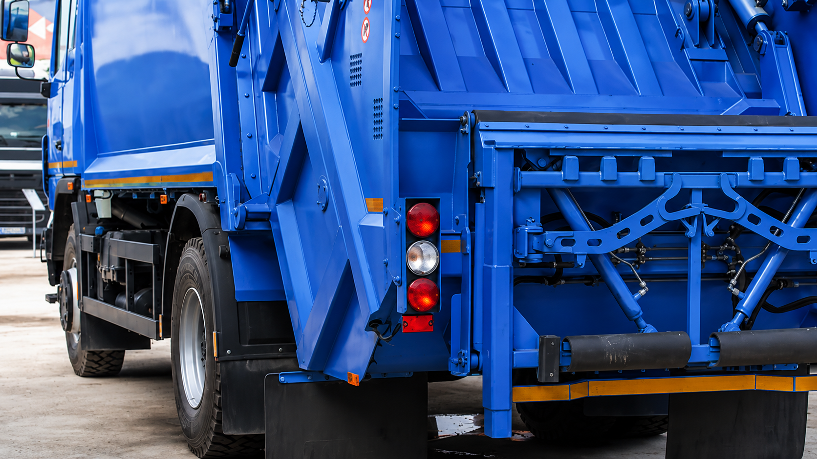Bright green garbage truck rear view on a street, with hydraulic lifting mechanism visible.