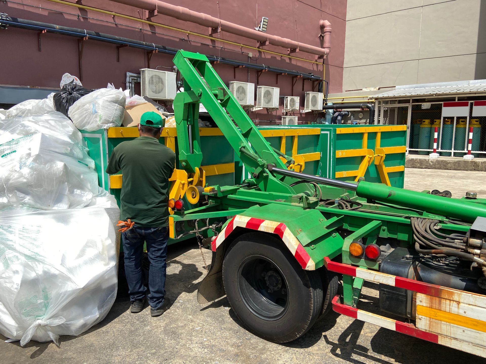 Worker beside green heavy machinery and large white bags in an industrial yard