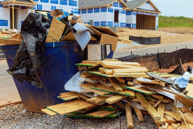 Blue dumpster overflowing with construction debris and lumber at a house build site