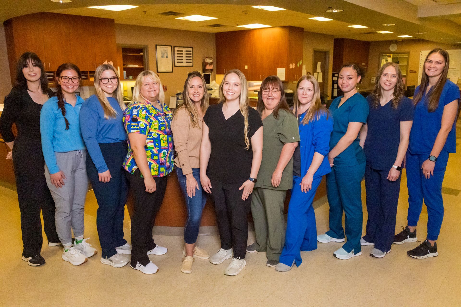 Group of healthcare workers in various scrubs, smiling, posing in a reception area.