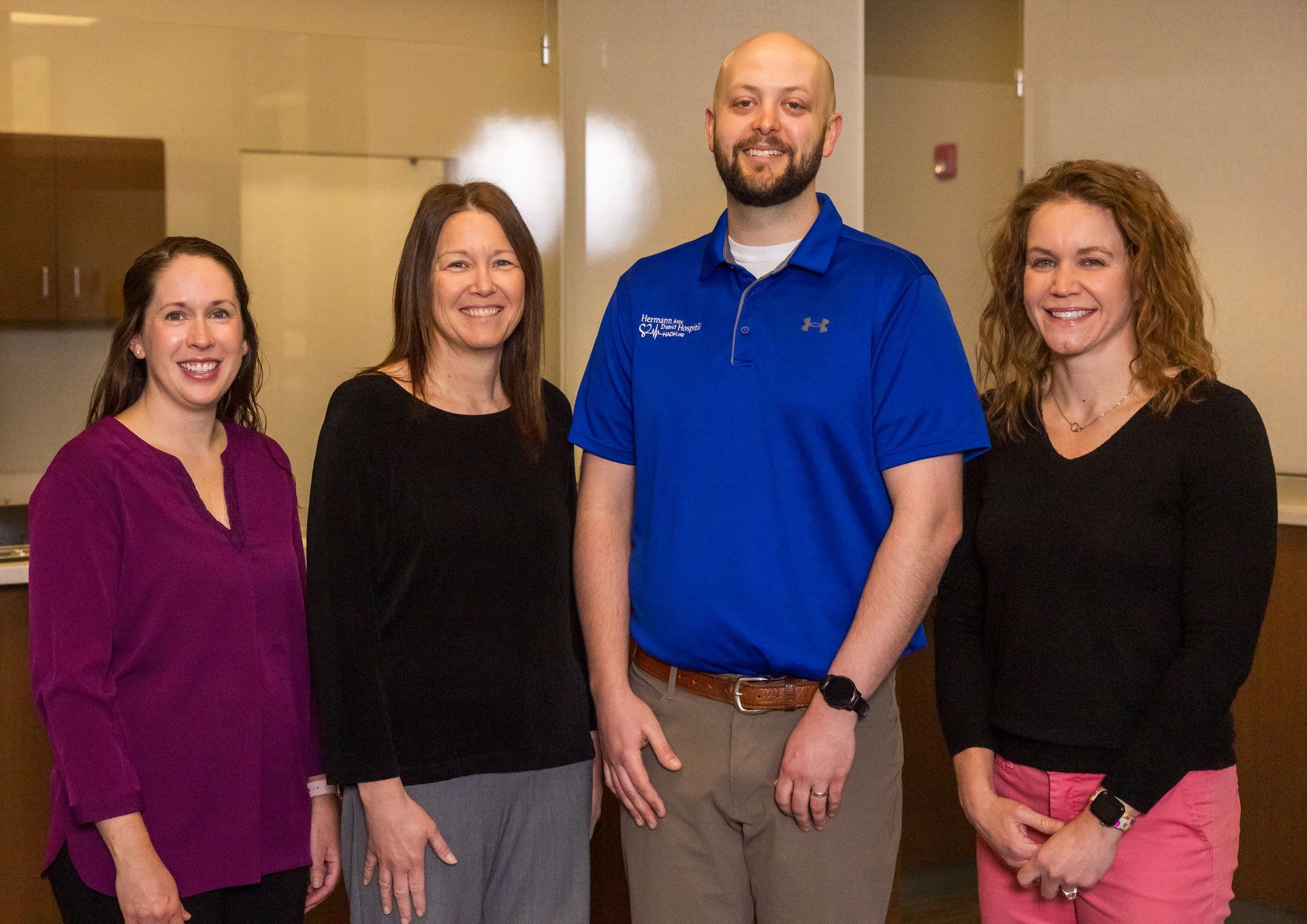 Four people standing in an office. A man in blue shirt, two women, and another woman, all smiling.