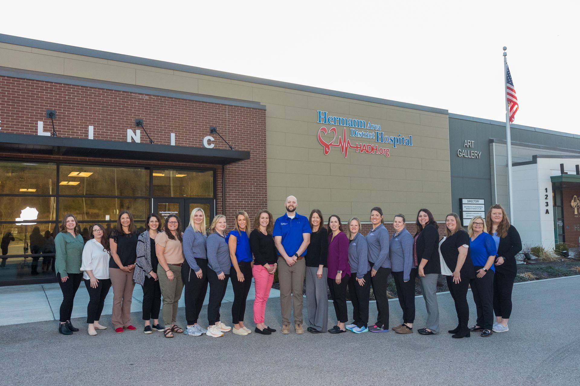 Staff outside a clinic with blue and red logo and American flag. Group poses in front of building.