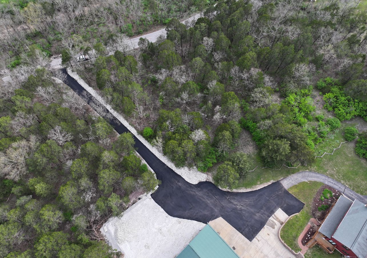 Aerial view of a wooded area beside a paved driveway and parking lot near a building