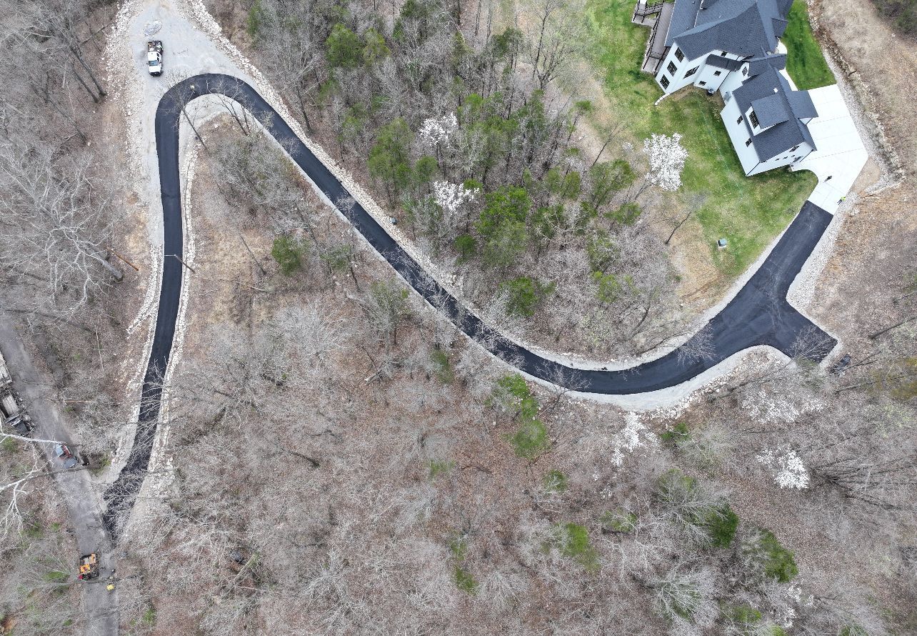 Aerial view of a winding driveway through leafless trees beside a house and paved turnaround area.