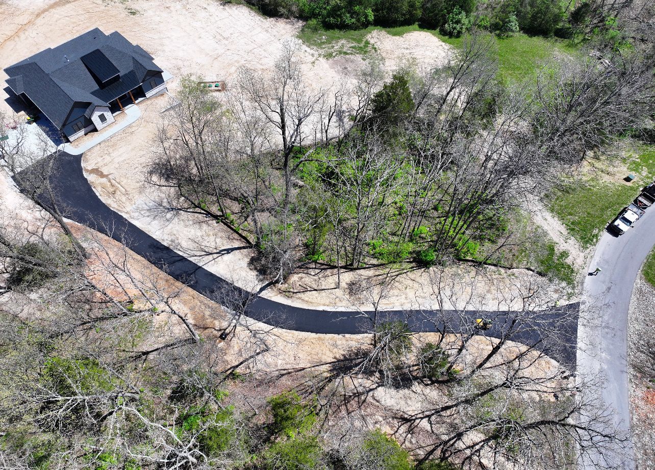 Aerial view of a house beside a curved driveway through leafless trees and patchy grass.