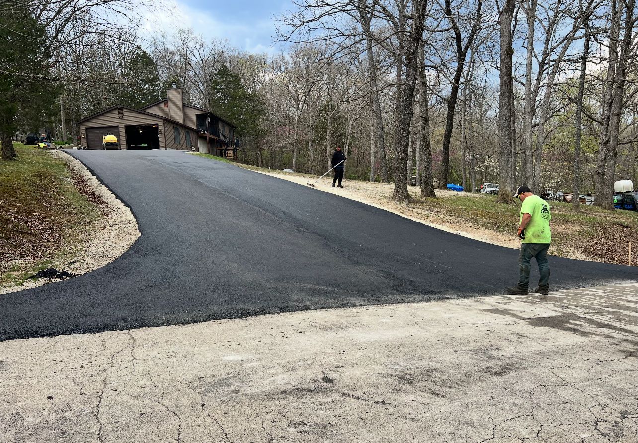 Freshly paved driveway on a wooded hill with two workers near a building entrance