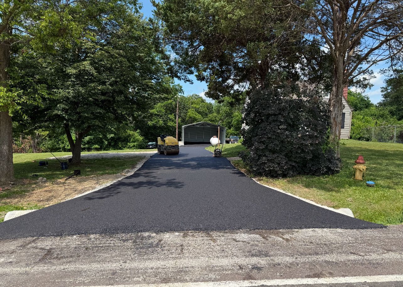 Fresh black gravel driveway leading to a house, framed by green trees and lawn.