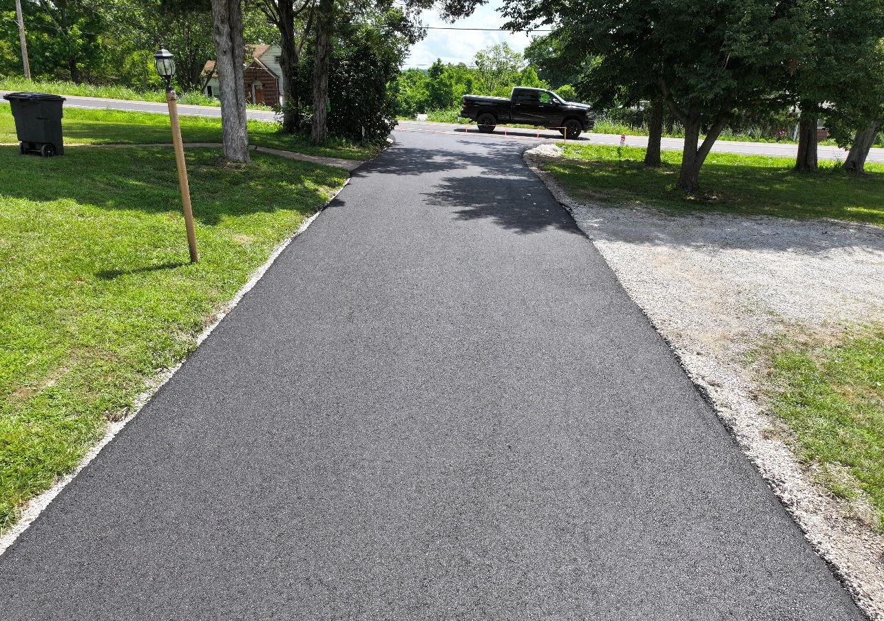 Paved path through a green park with trees and gravel, leading toward picnic tables in the distance