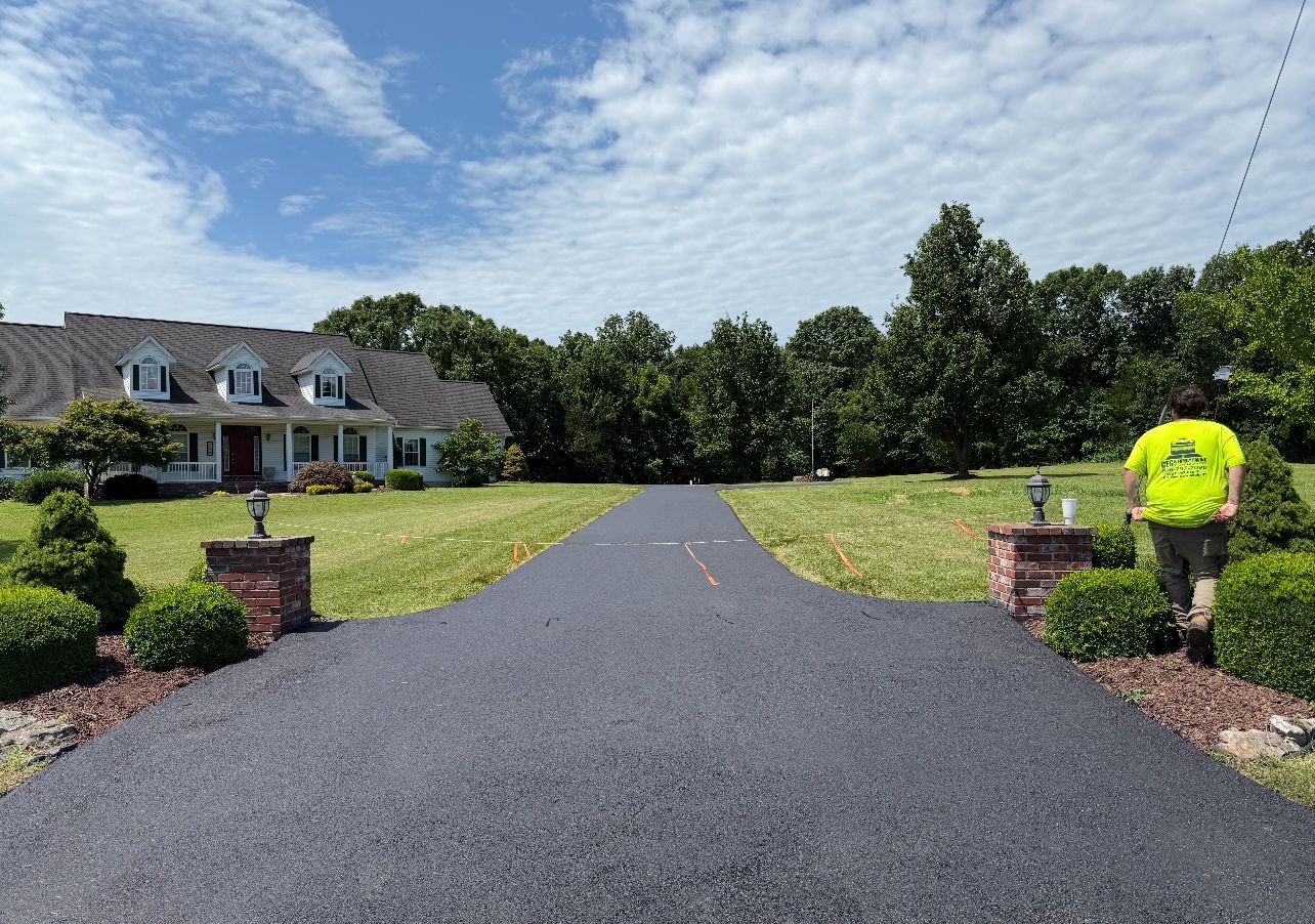 Freshly paved driveway leading to a large house, with a worker in a neon shirt on the right.