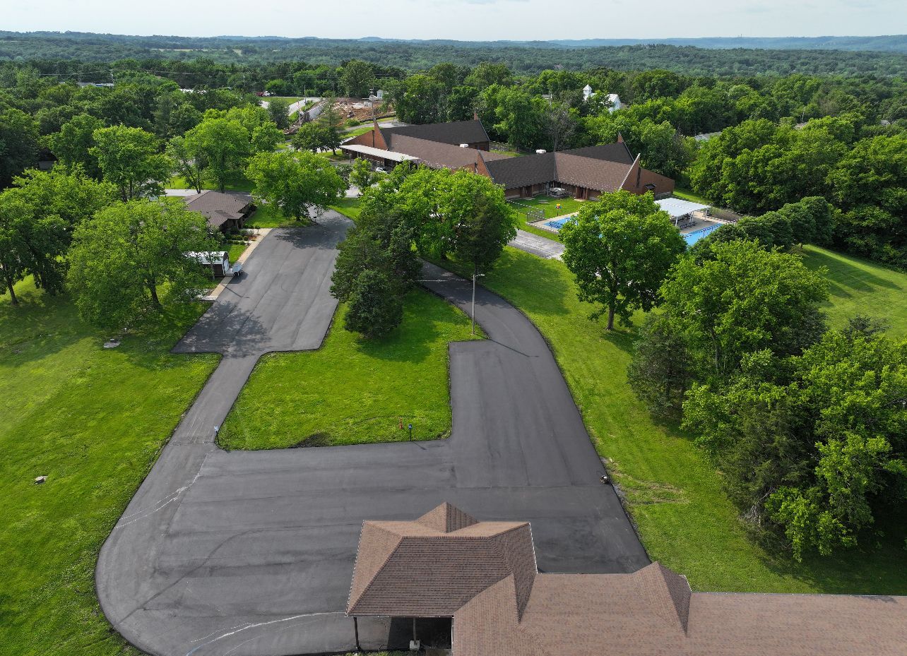 Aerial view of a paved road leading to a house surrounded by lush green trees.
