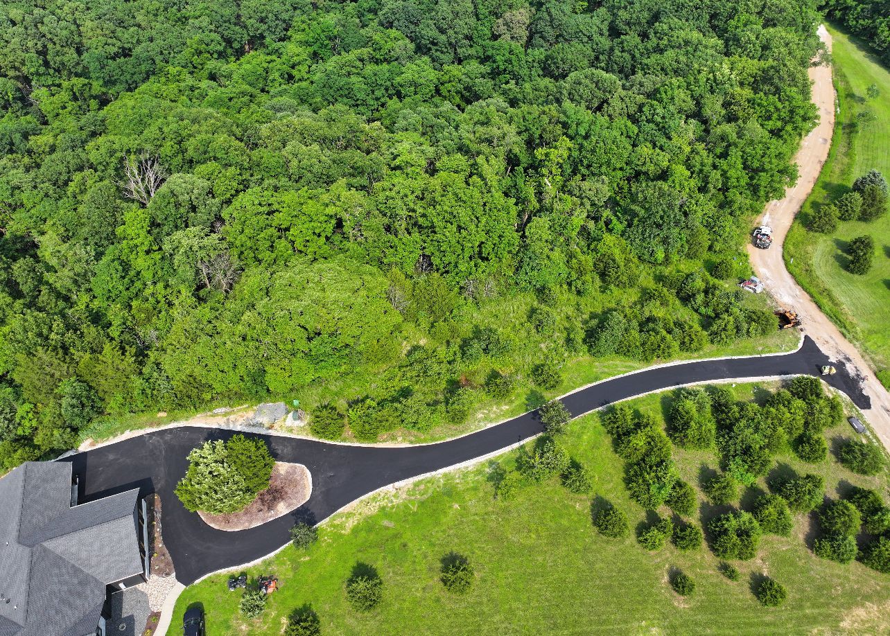 Aerial view of a winding road through dense green forest and grassy landscaping.