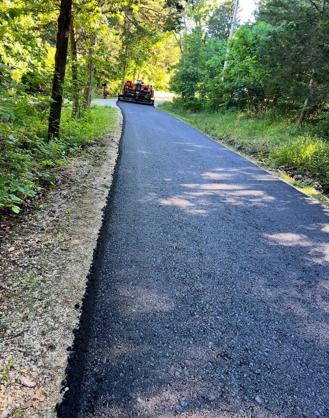 Paved road through a wooded area with a vehicle ahead in the distance.