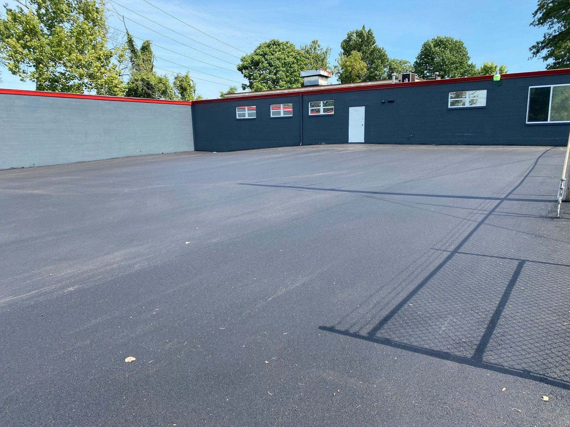 Empty asphalt parking lot beside a dark building with small windows and a white door.