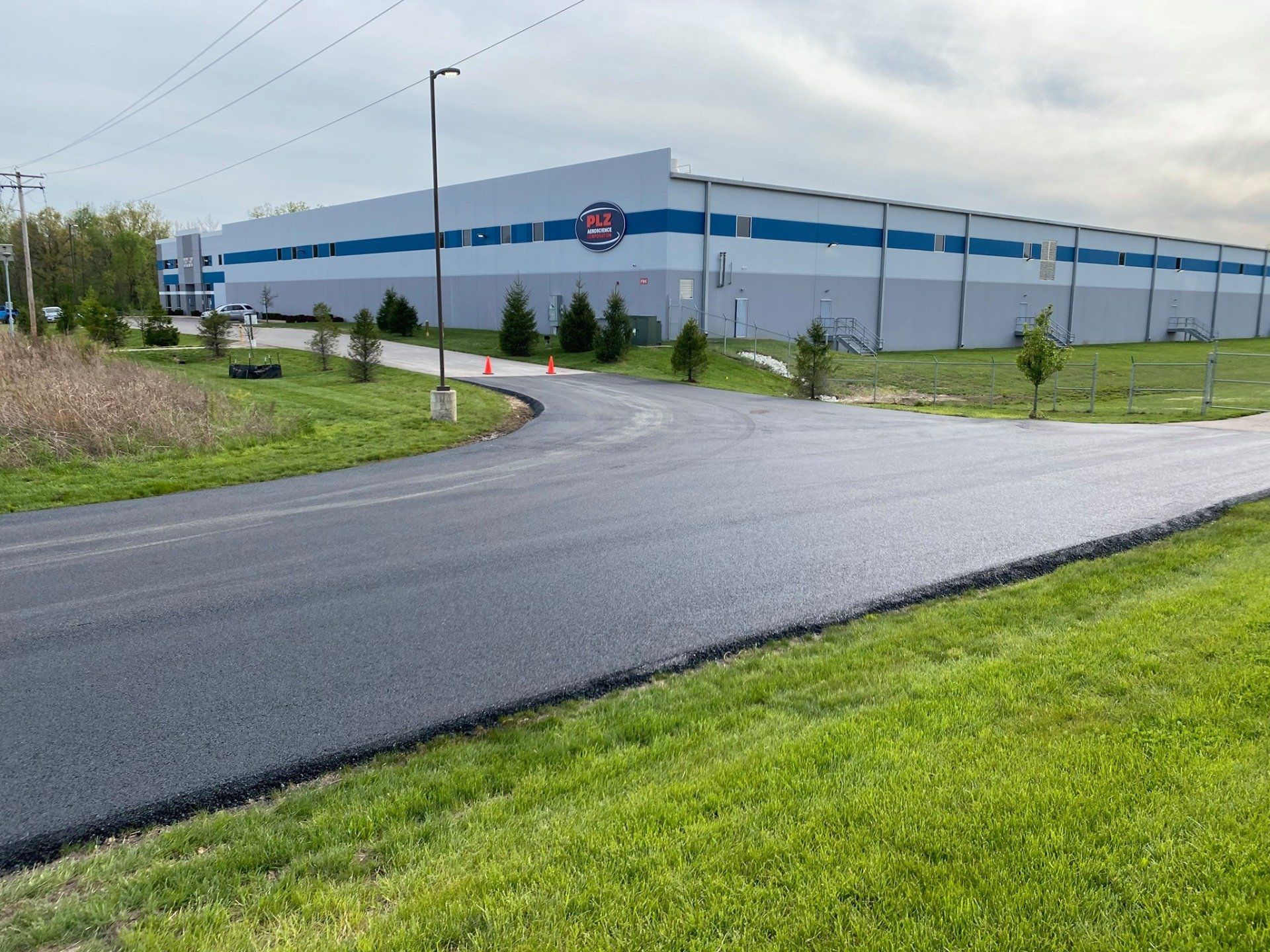 Curved paved road beside a large white warehouse with blue stripes on a cloudy day