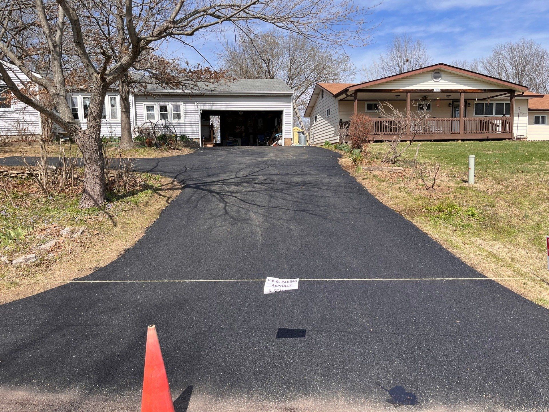Long driveway leading to a white garage and a brown house on a grassy suburban property