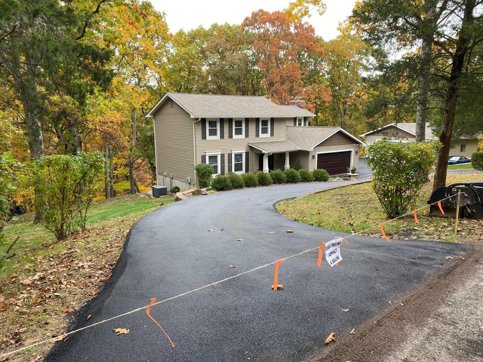 New asphalt driveway leading to a house with autumn trees and survey markers.