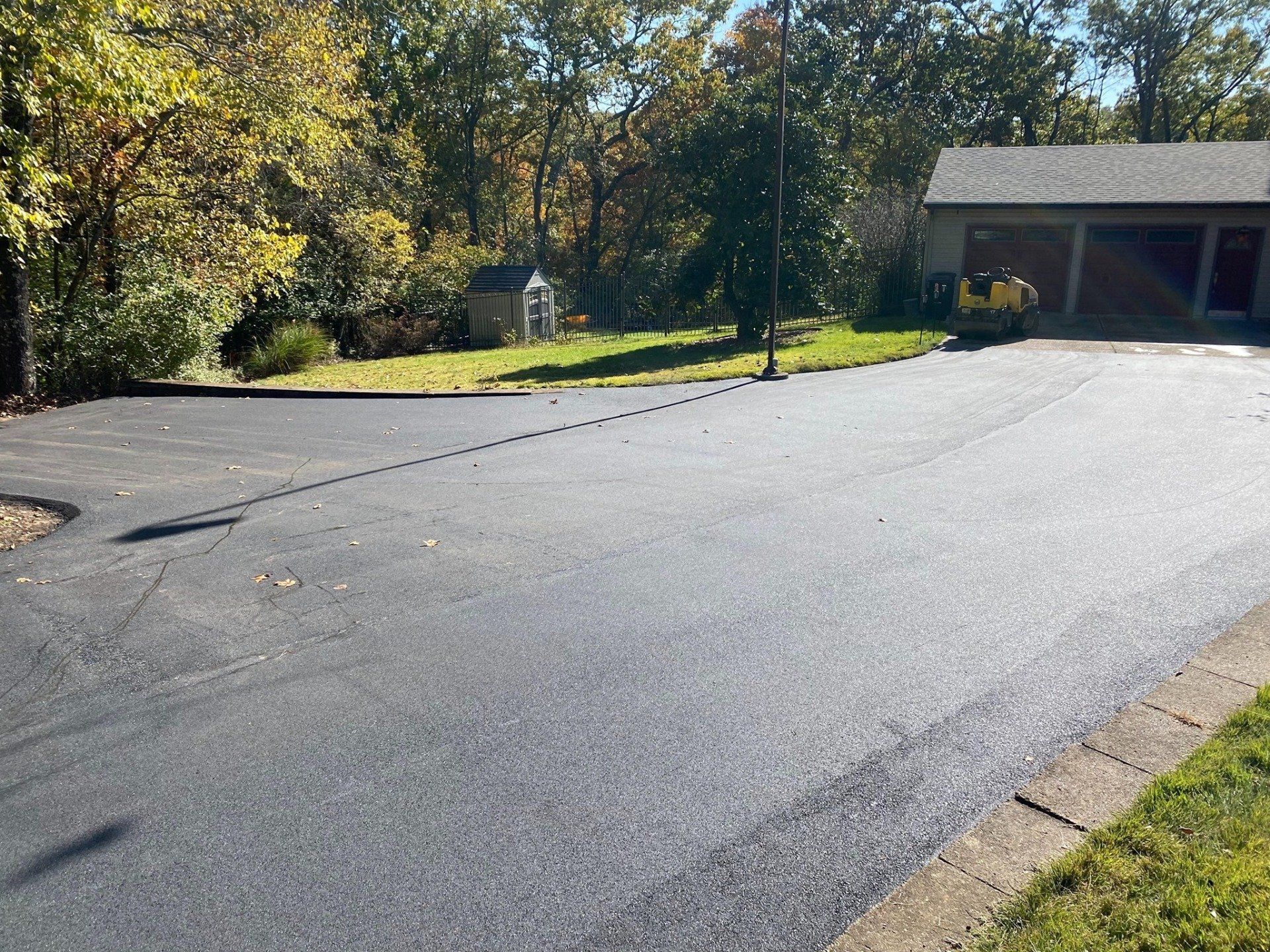 Quiet suburban driveway with a wide asphalt surface, trees, and a house garage in the background