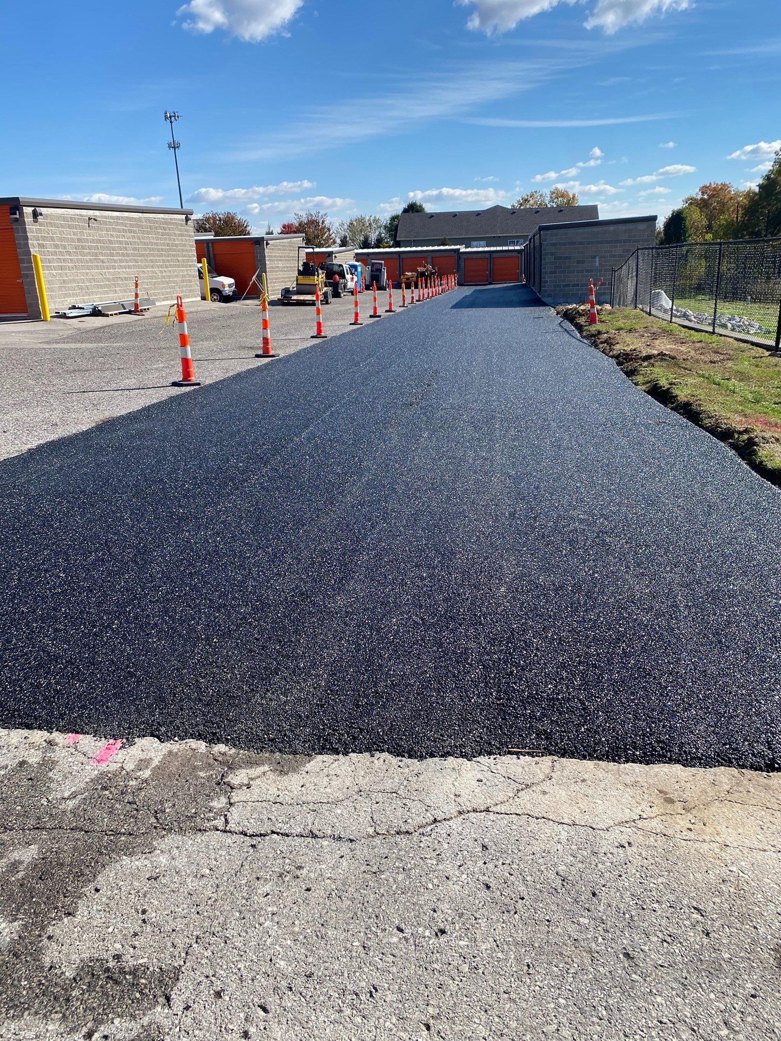 New blacktop driveway under construction with orange cones beside stone buildings and blue sky