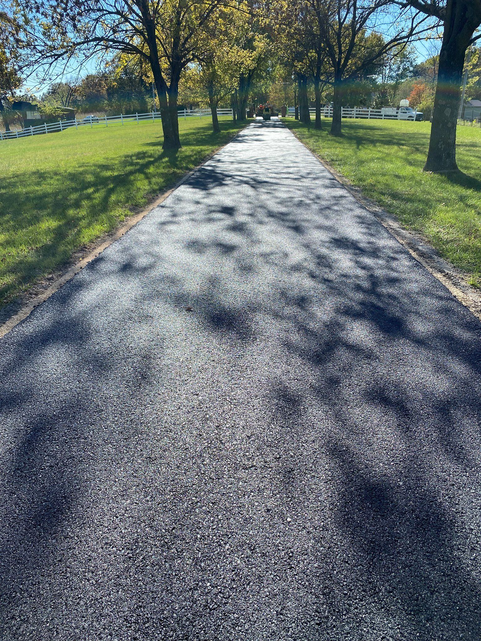 Sunlit gravel path through a grassy park with trees on both sides