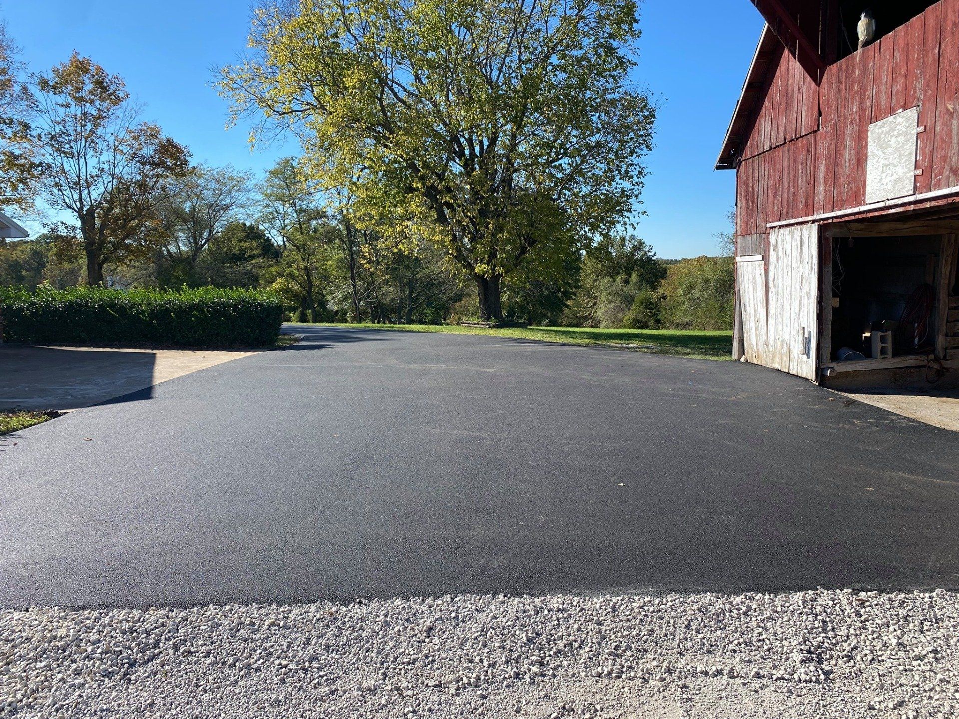 Freshly paved driveway beside a red barn on a sunny day with trees in the background