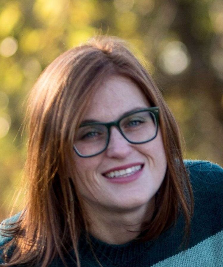 A woman wearing glasses and a striped sweater is smiling for the camera.