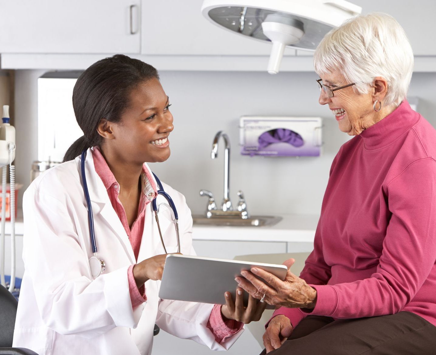 A doctor is talking to an older woman who is holding a tablet