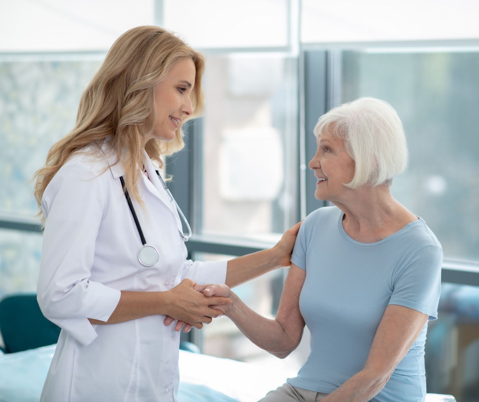 A doctor is shaking hands with an elderly woman in a hospital room.