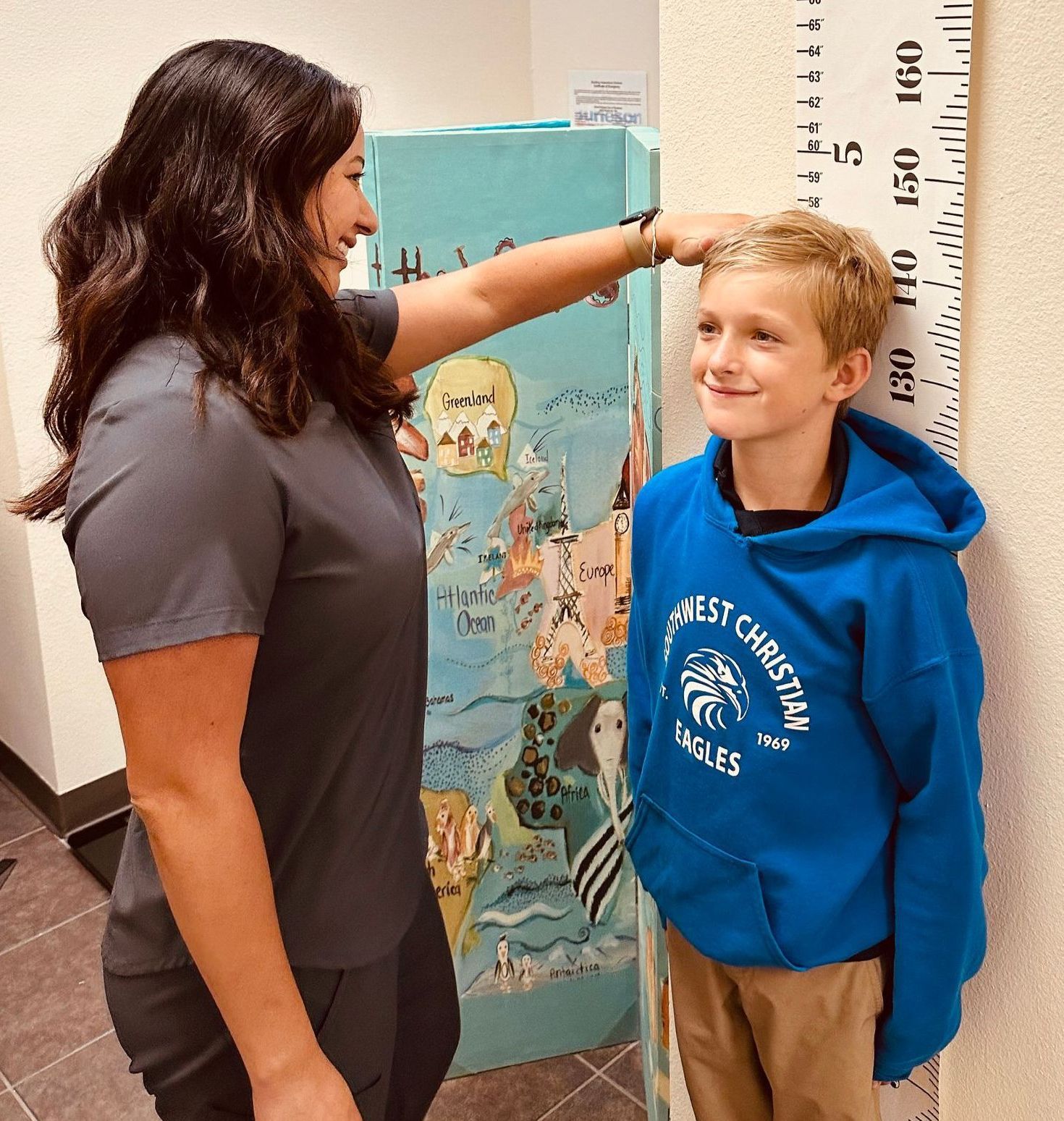 A woman is measuring a boy 's height with a ruler