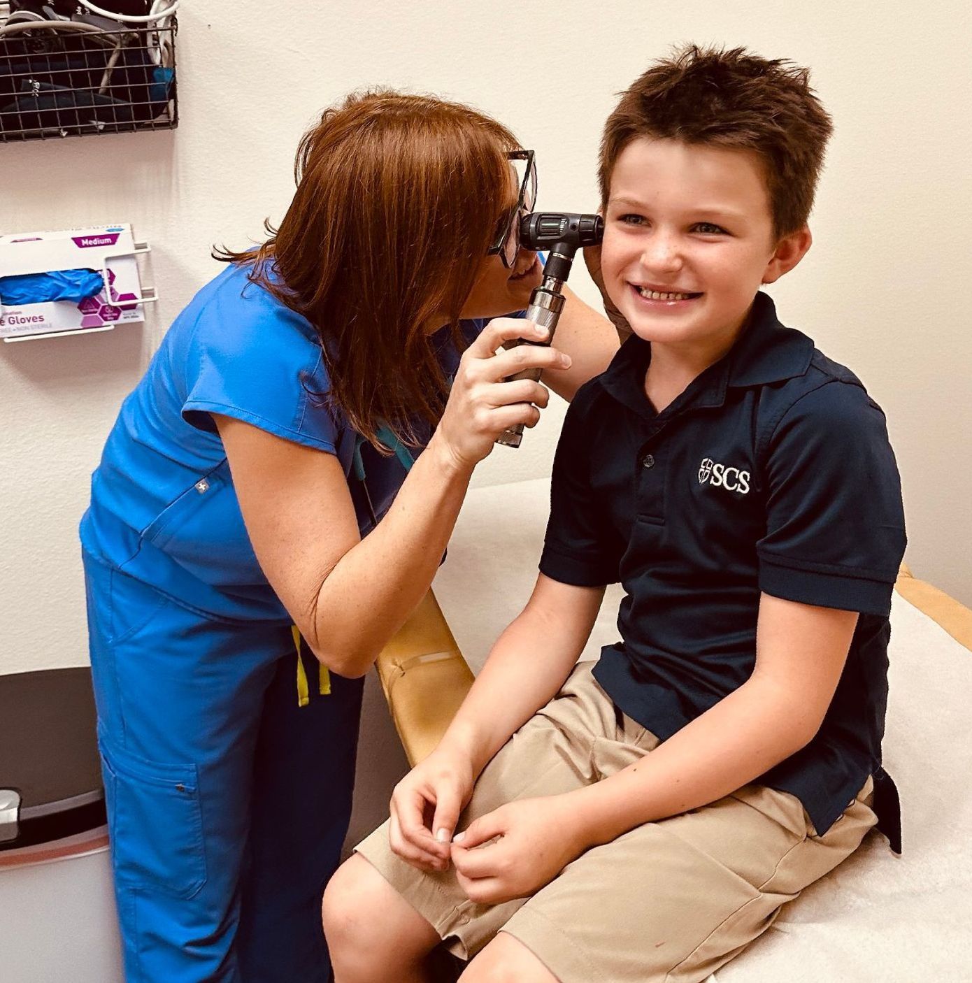 A woman is examining a young boy 's ear with an otoscope