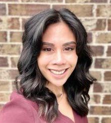 A woman is smiling in front of a brick wall.
