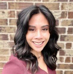 A woman is smiling in front of a brick wall.