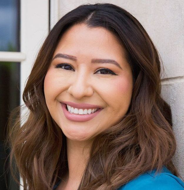 A woman is smiling for the camera while leaning against a wall.